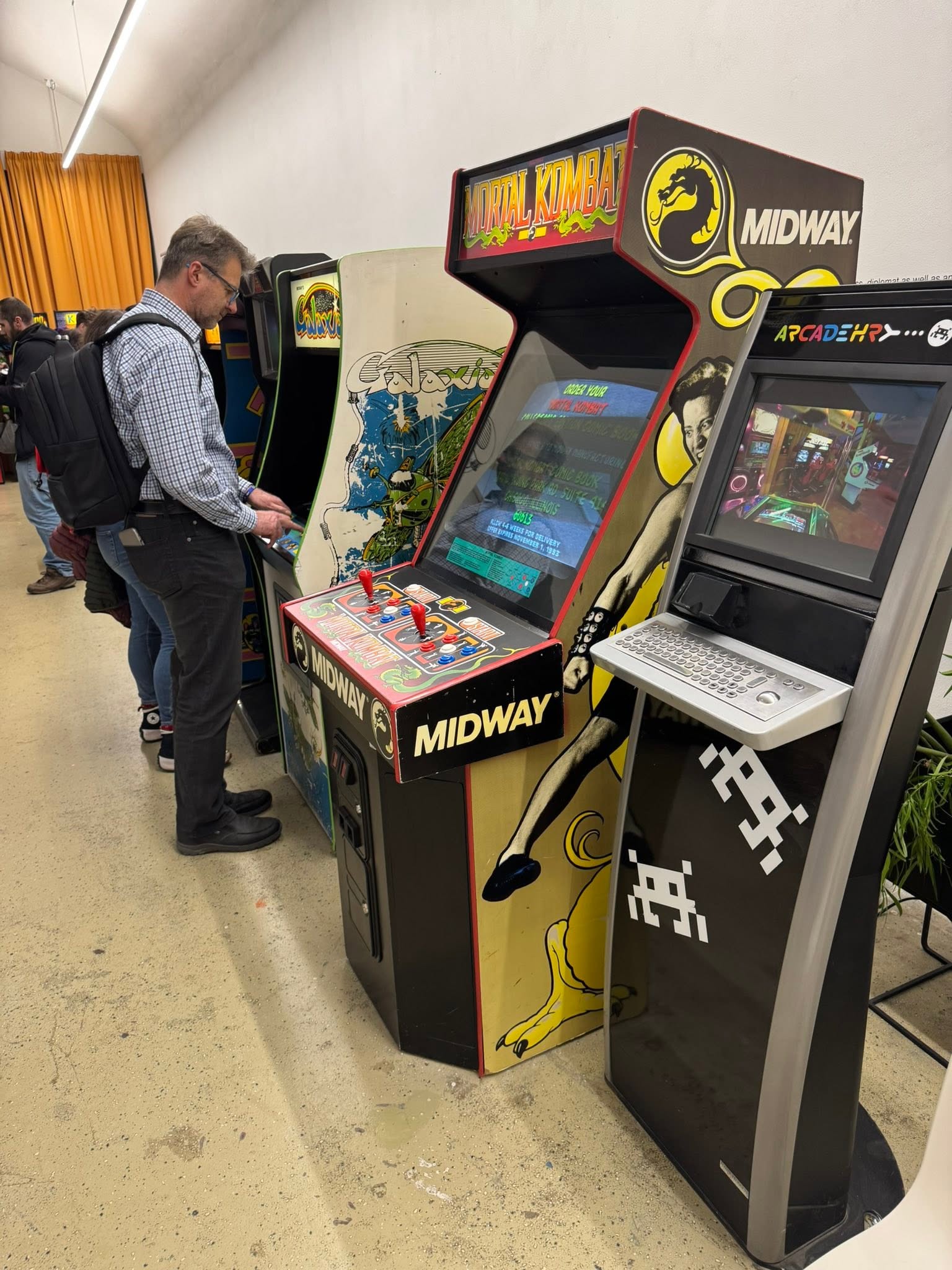 Návštěvník hraje na arkádovém automatu Mortal Kombat vedle dalších skříní.